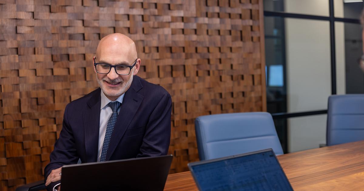 Man in a suit sitting at a conference table with a laptop.