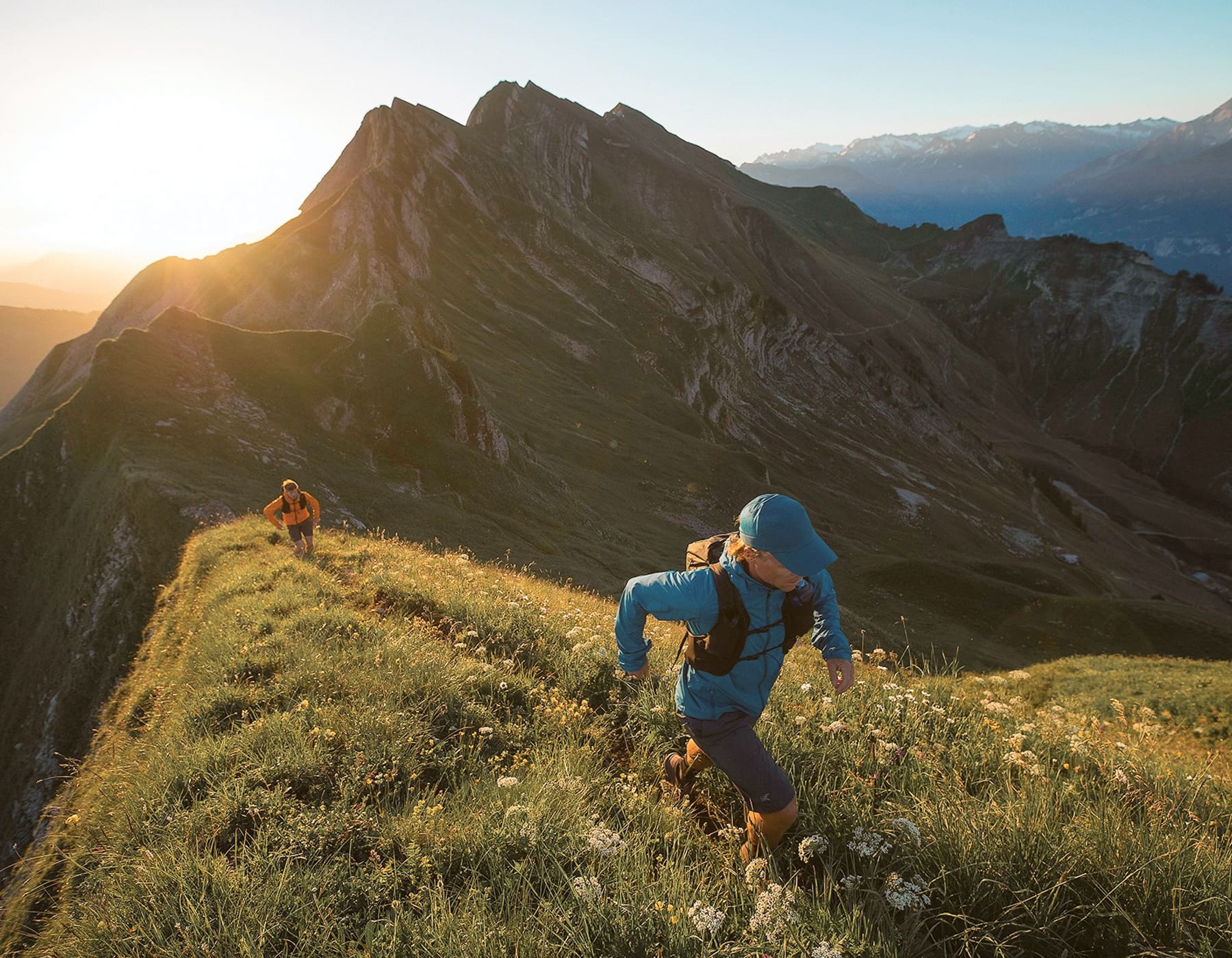 Kelowna hiking gear. Two runners with hydration packs and running jackets going up a grassy mountain during sunset