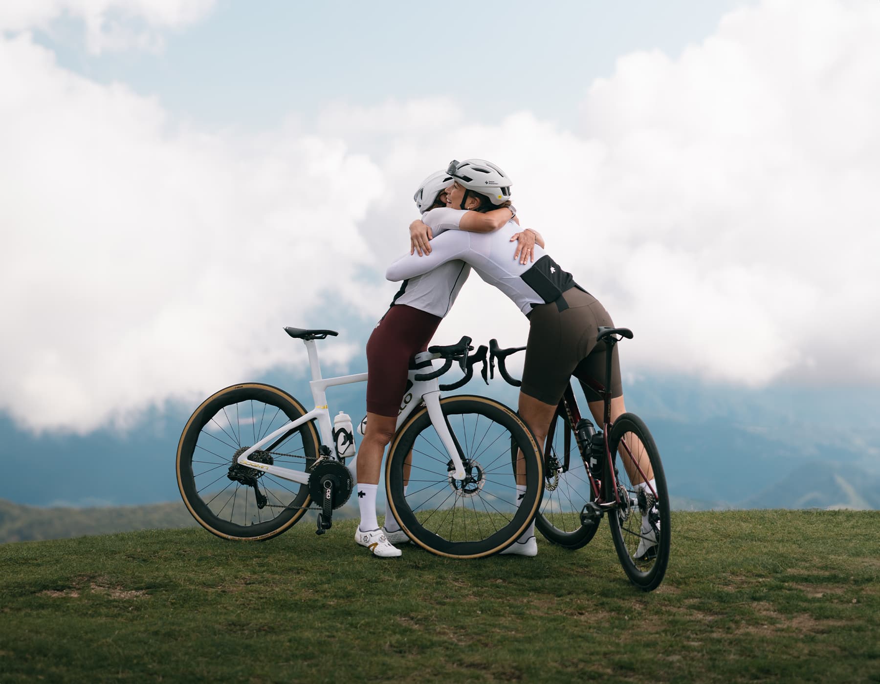 Two women wearing ASSOS premium cycling apparel riding road bikes through a beautiful green countryside