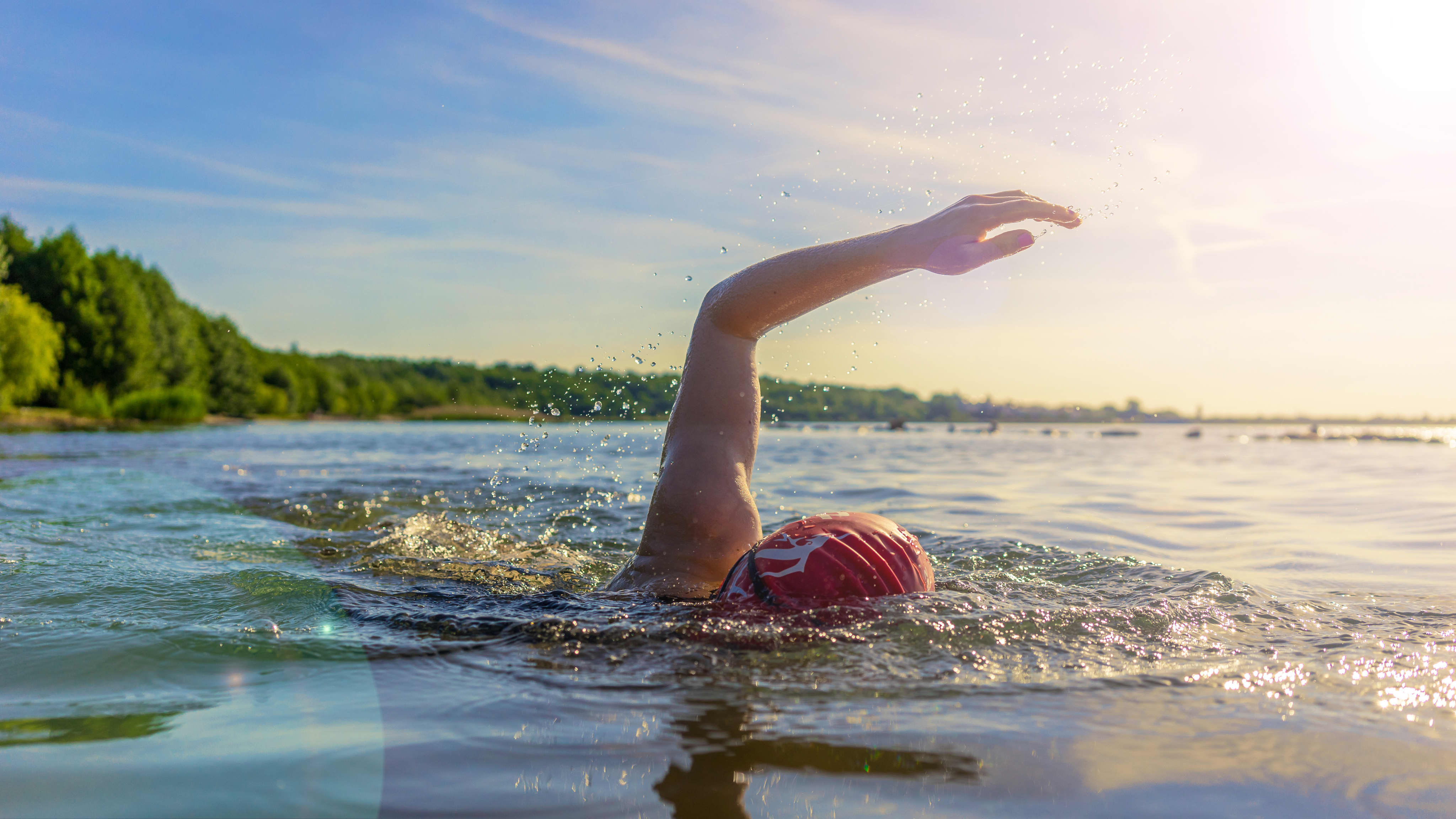 A swimmer's arm reaches out mid-stroke, wearing a bright red swim cap, one of the simplest pieces of visibility gear for open water swimming.