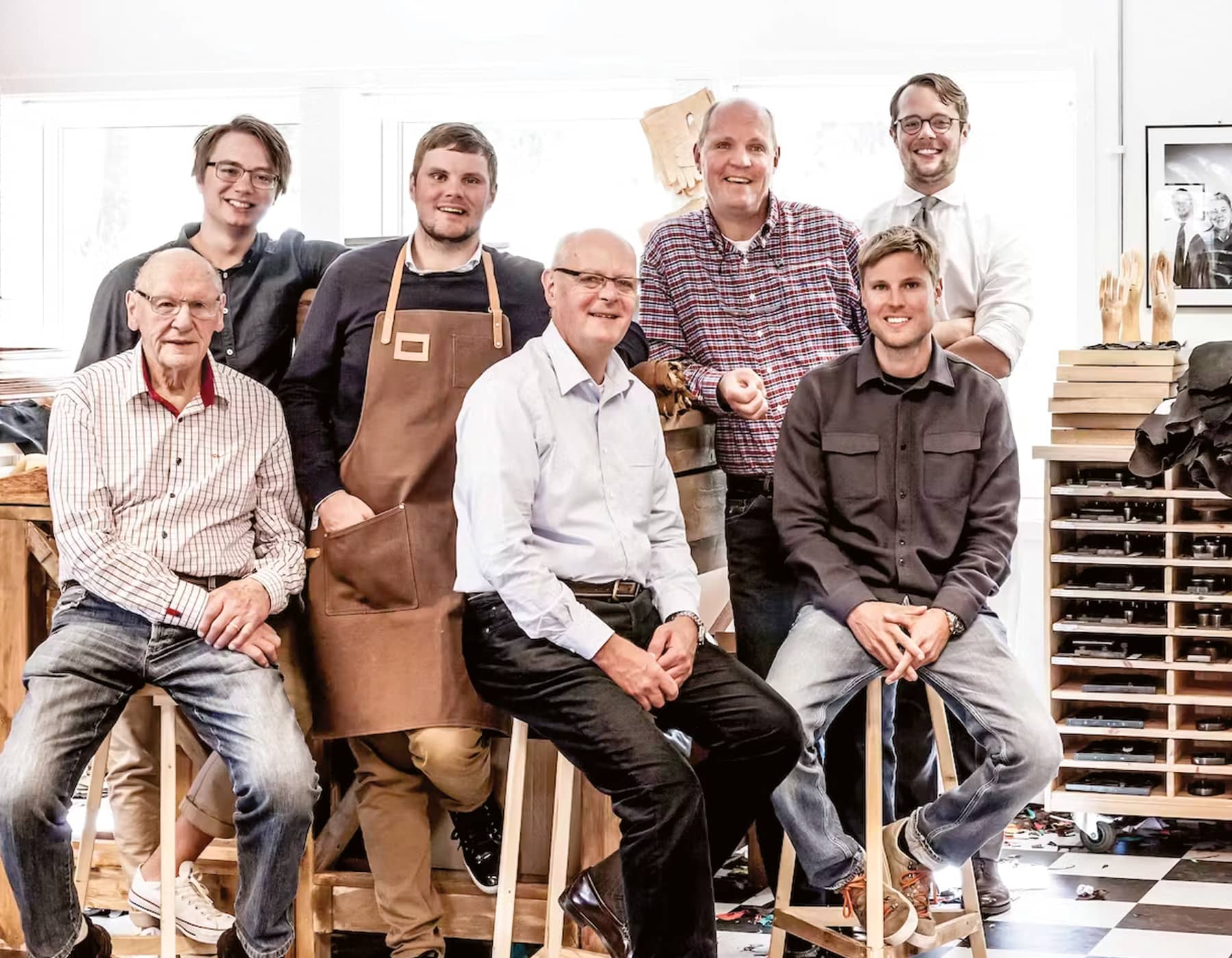 7 members of the Martin Magnusson & Co family who originated and continue to operate Hestra, in one of their workshops sitting on stools an standing for a photo. 