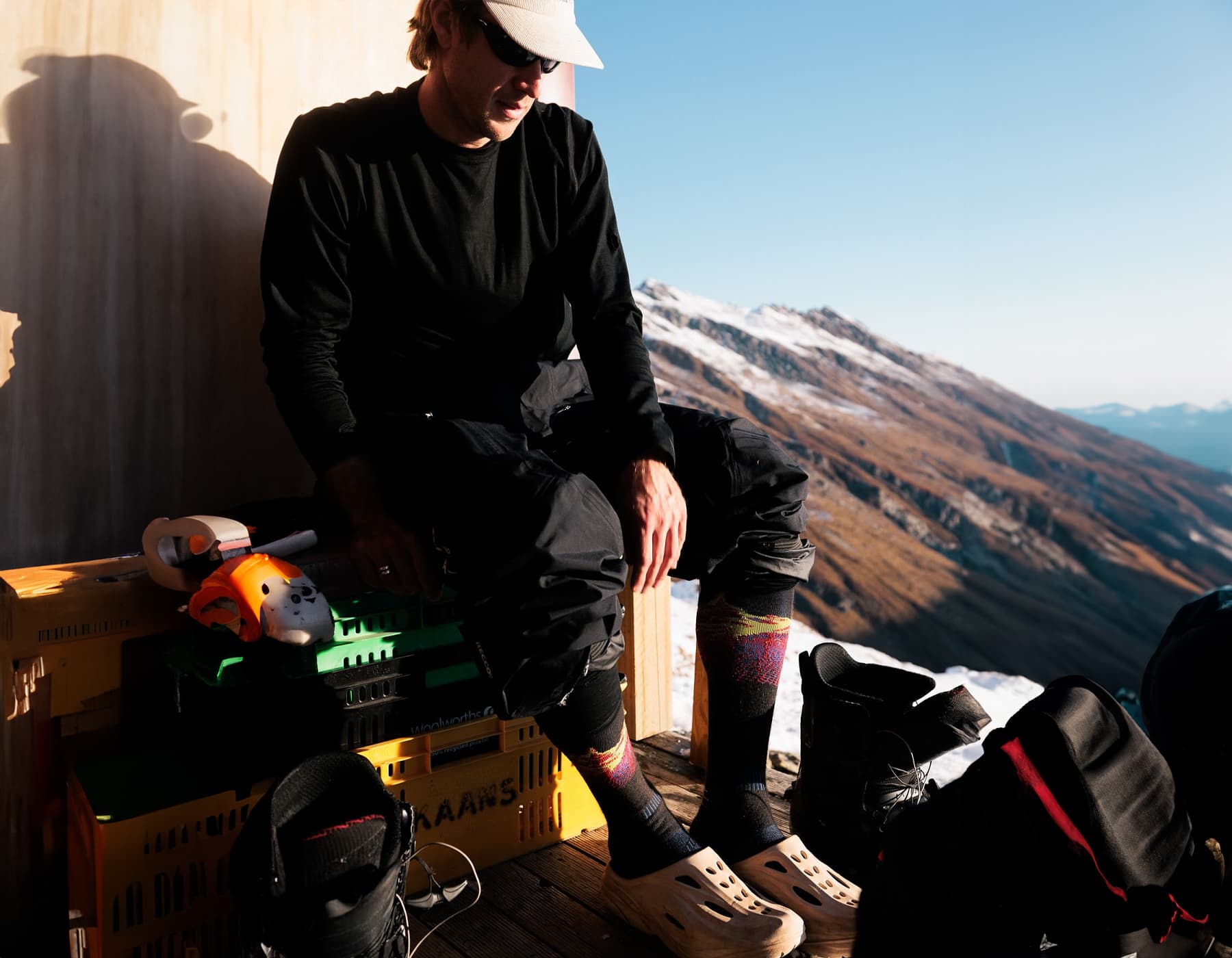 Man sitting in a mountain lodge with ski boots off, wearing LÉ BENT merino wool socks and enjoying the alpine view