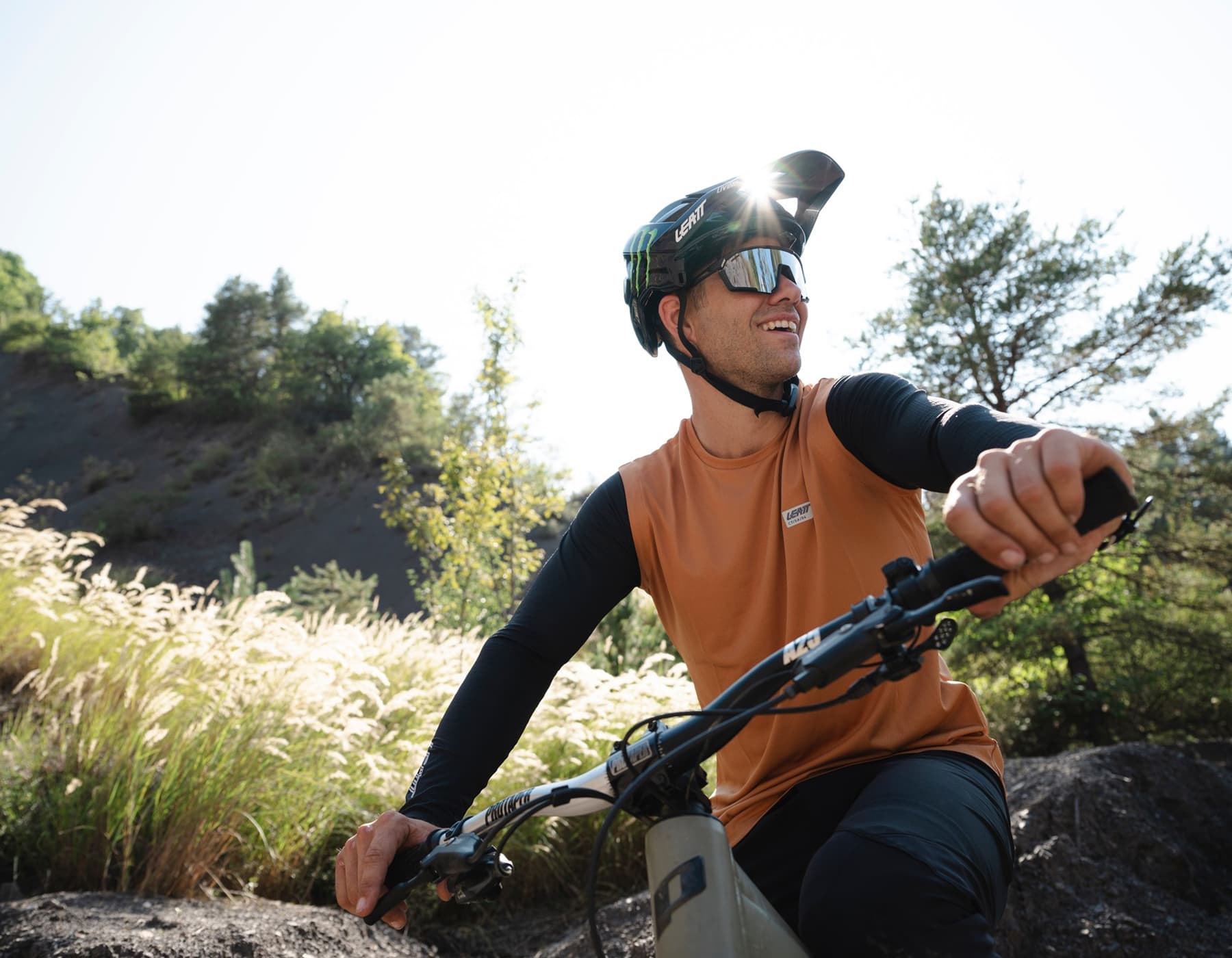 MTB rider wearing Leatt jersey and helmet pausing on bike overlooking scenic landscape