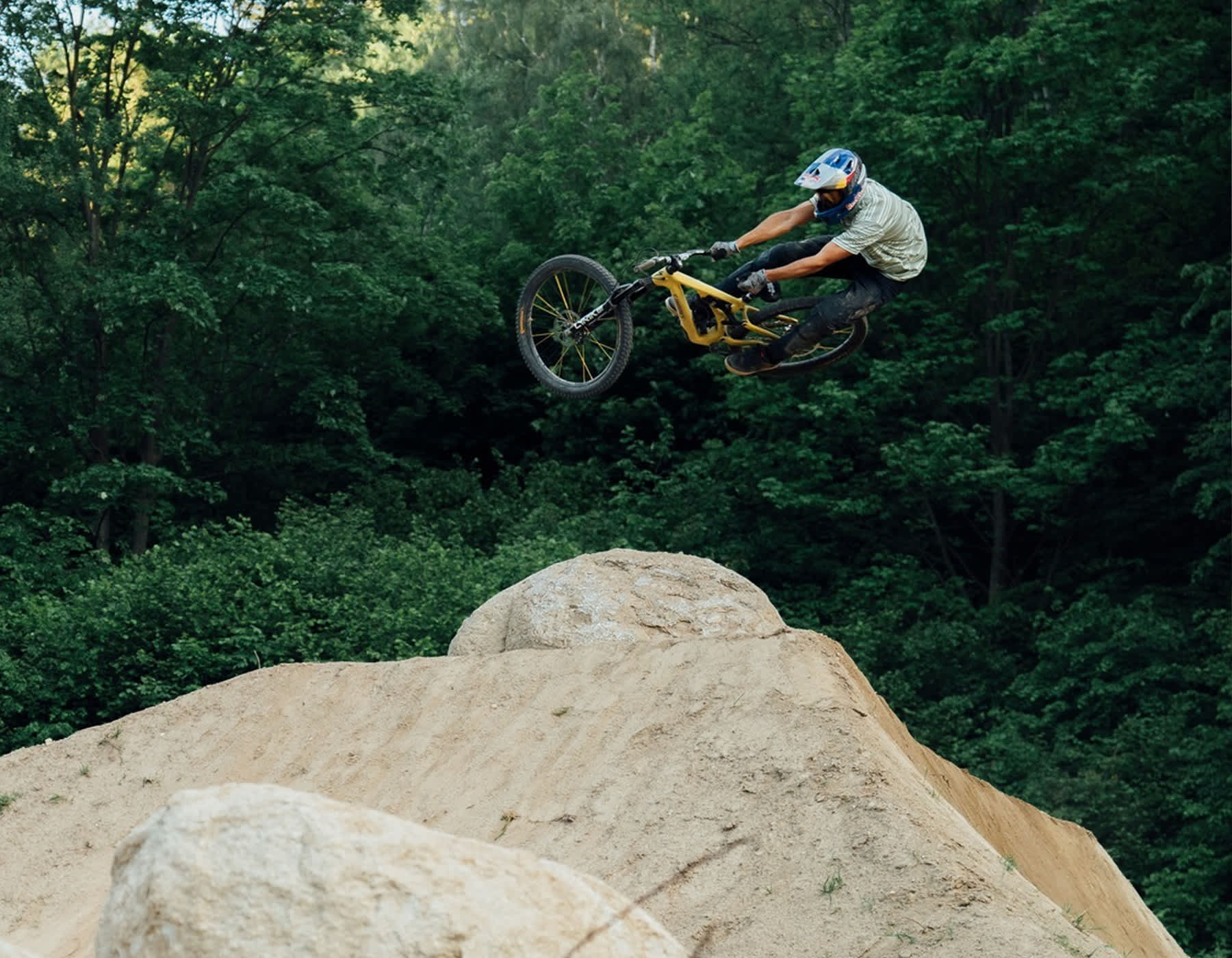 Downhill mountain biker mid-jump in Leatt full face helmet and gloves on dirt trail