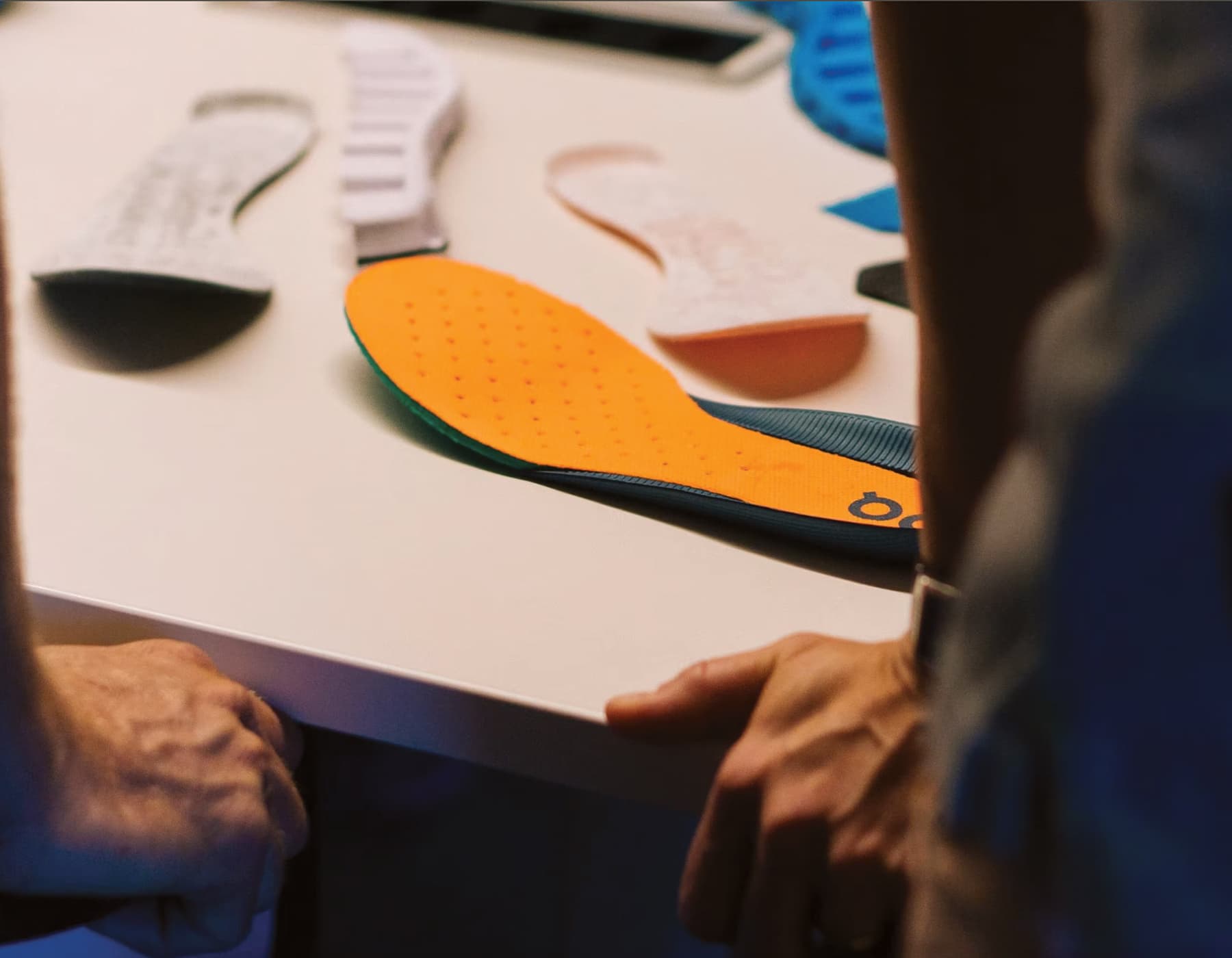 A birds eye view of a table with different shoe insole prototypes on top. Two people viewing down at these with their faces out of the shot. 