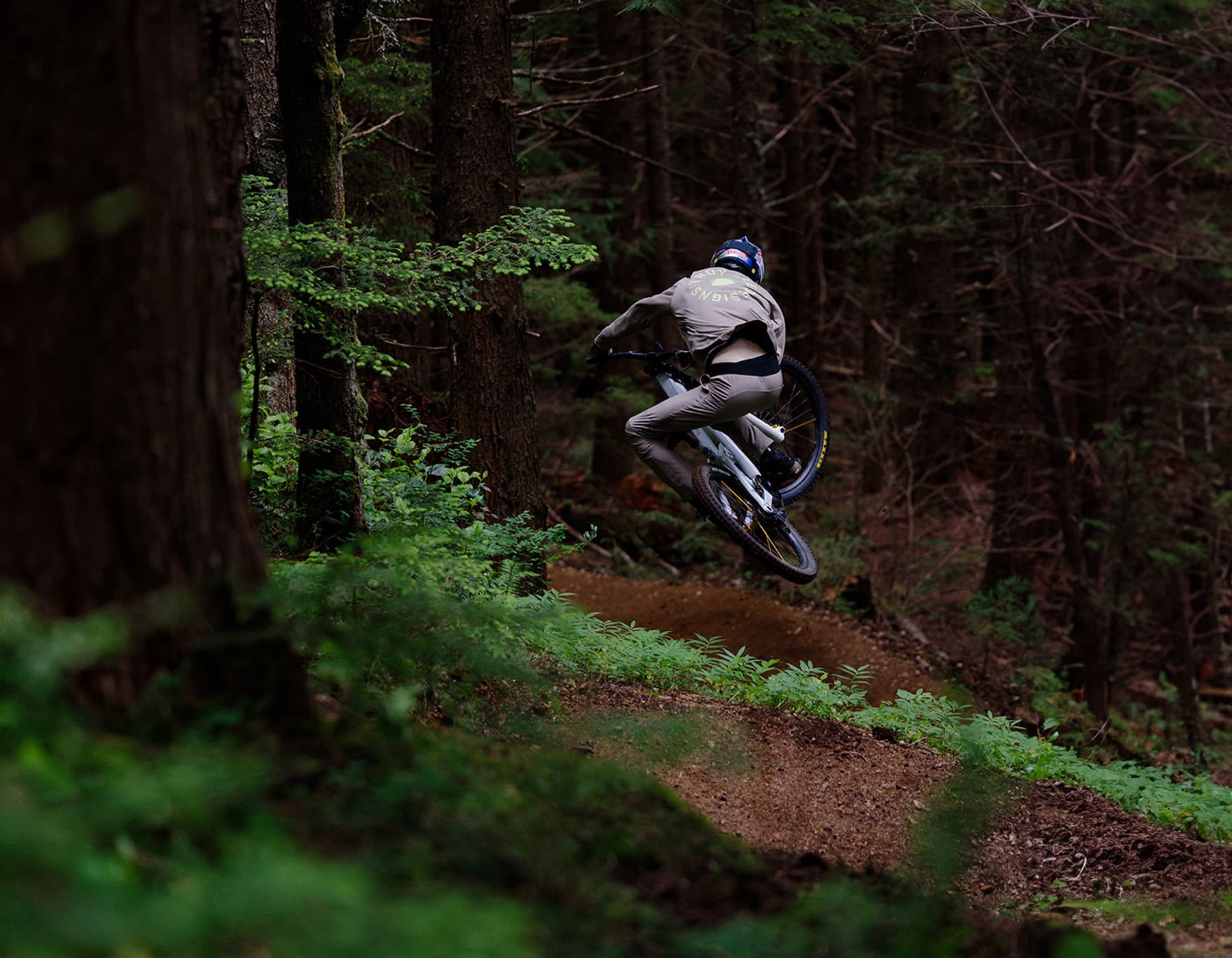 Mountain bike rider wearing Troy Lee Designs apparel, helmet, and gloves jumping on dirt trail