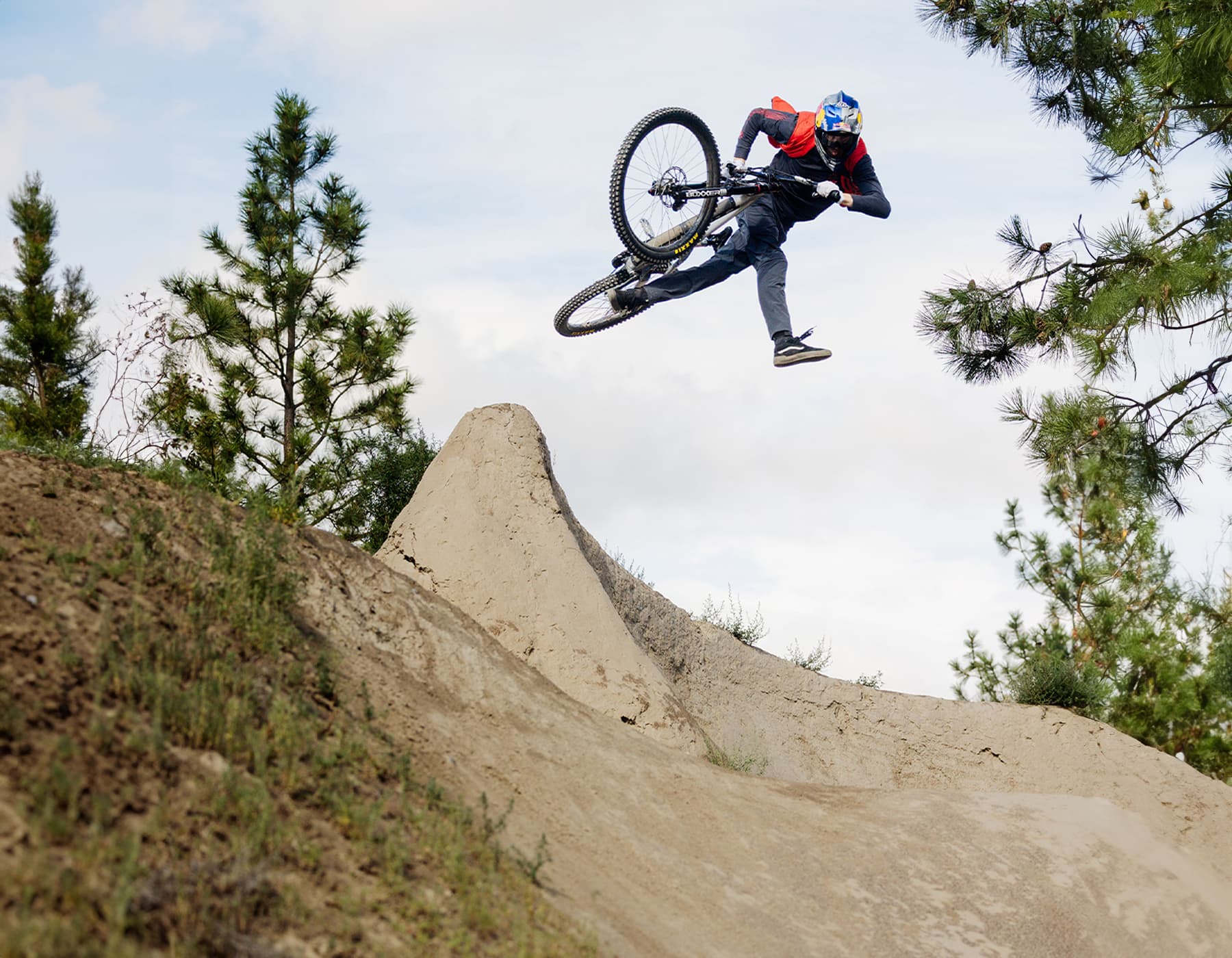 Mountain bike rider wearing Troy Lee Designs apparel, helmet, and gloves jumping on dirt trail
