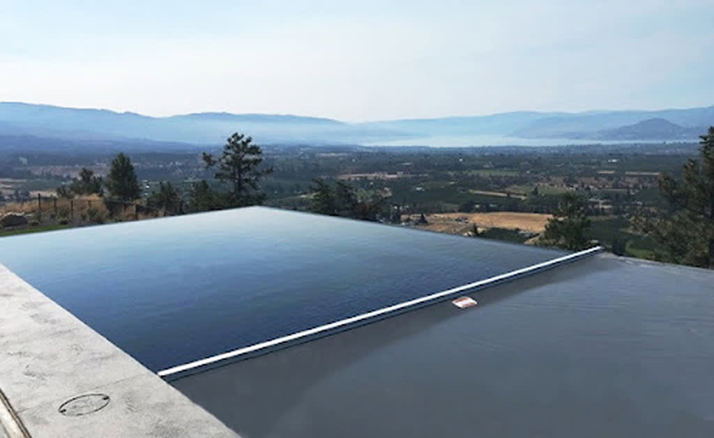 An infinity edge pool cover closes over a pool in the Okanagan. An automatic pool cover is a must-have for pool safety, maintenance, and more.